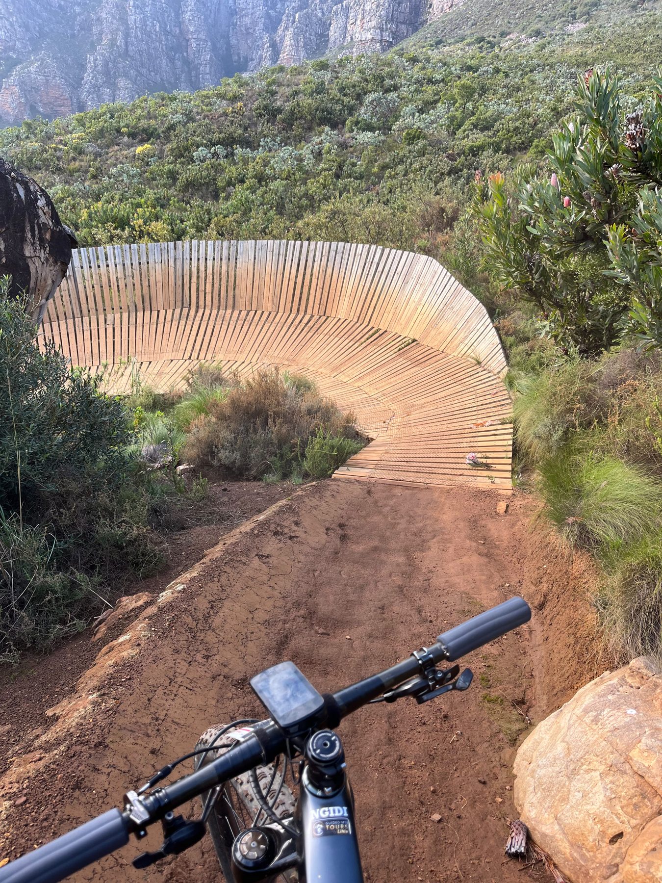 Handlebar view of a bermed dirt descent on a Stellenbosch mountain bike trail